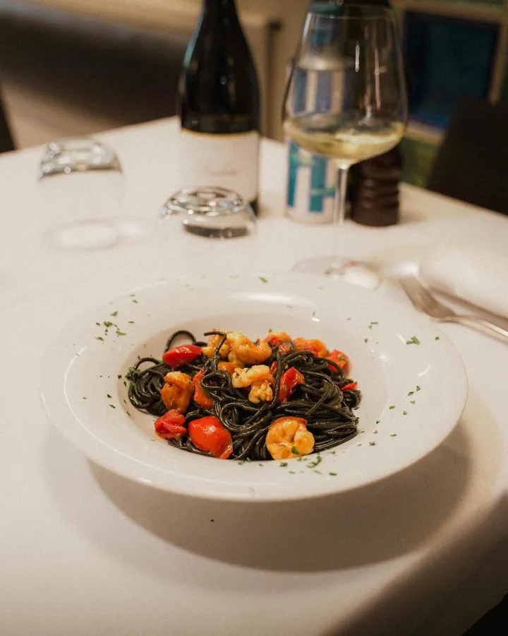 Spaghetti al nero di seppia con gamberi e pomodorini, serviti in tavola