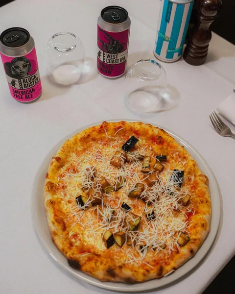 Pizza con formaggio grattugiato e cubetti di melanzana, con birre artigianali sullo sfondo